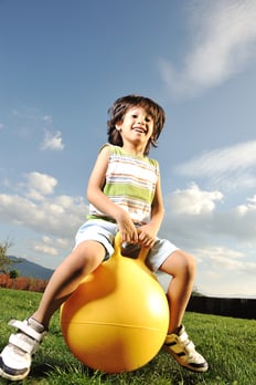 Little happy boy playing with big ball and jumping with slight motion up, scene in park