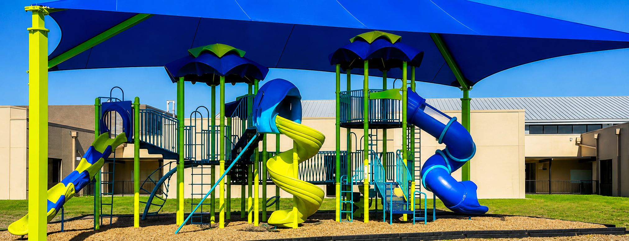 Colorful school playground with blue and green slides, climbing structures, and a large blue shade canopy at a Lamar CISD school.