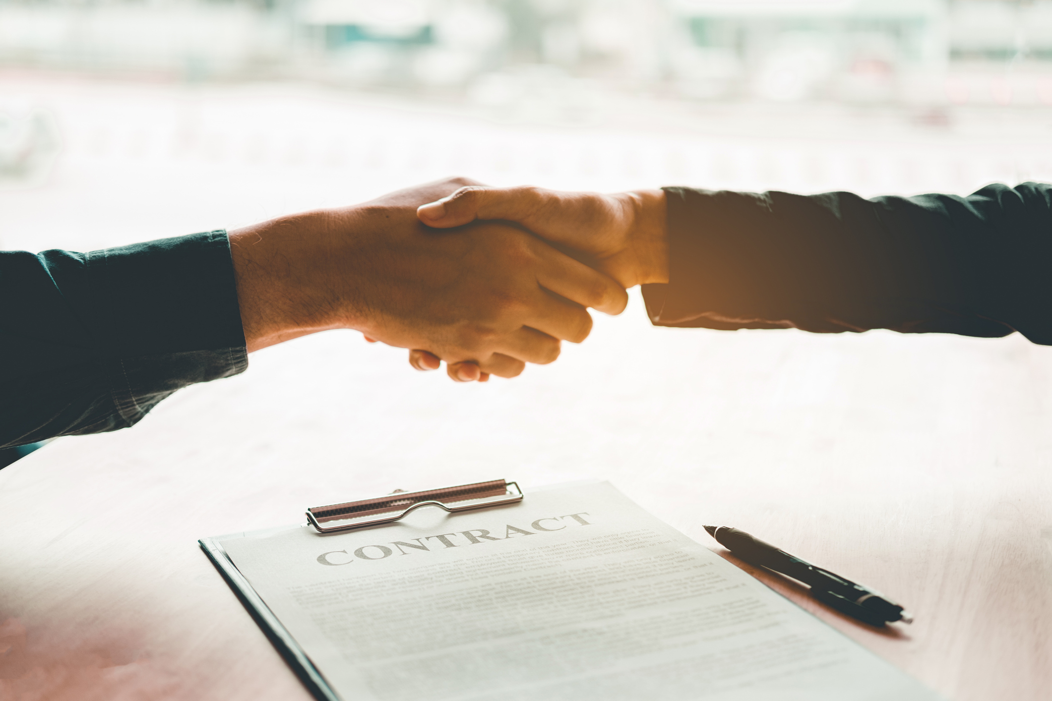 Two professionals shaking hands over a contract, representing cooperative purchasing agreements and competitive bidding for Texas school and city playground projects.