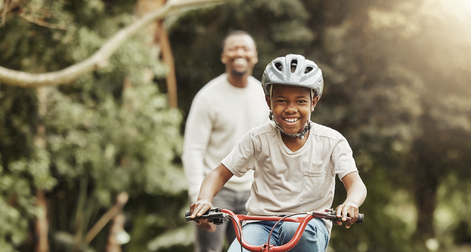 Young boy learning to ride a bicycle with his father outdoors